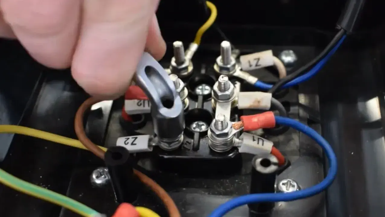 Main d'un technicien manipulant un connecteur sur un bornier électrique. Le moteur électrique chauffe et s'arrête, nécessitant une vérification des connexions.