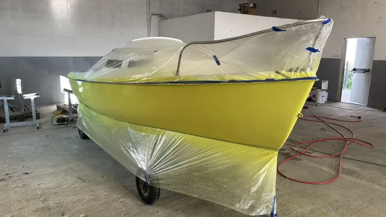Un bateau jaune est bâché pour le repeindre. Il est sur une remorque dans un atelier.