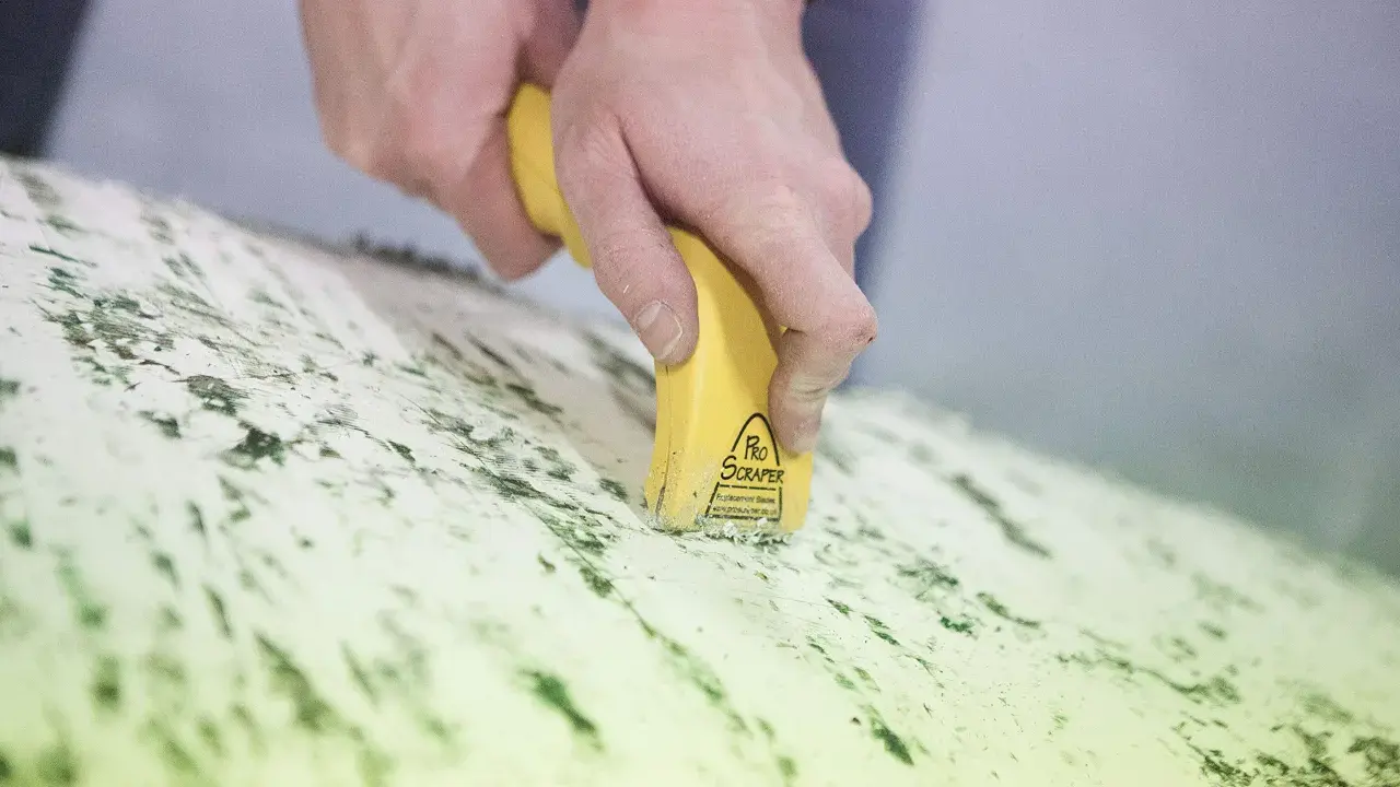 Mains utilisant un grattoir électrique antifouling pour enlever des résidus verts sur une surface.