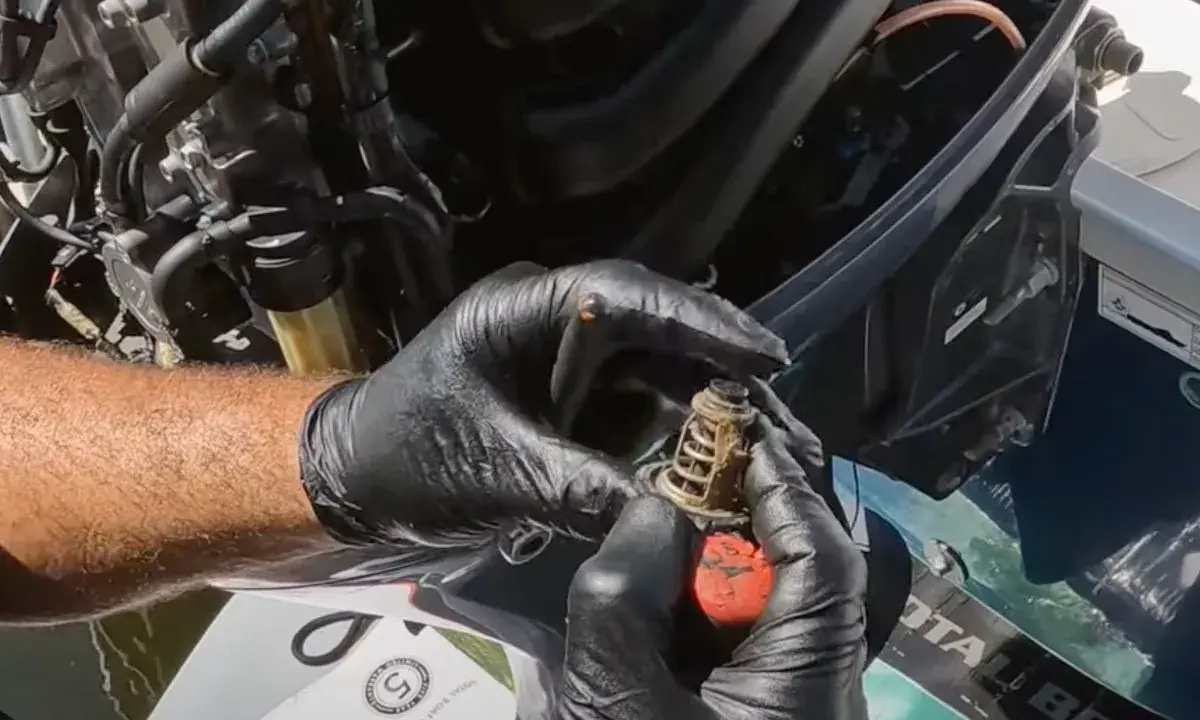 Mains gantées tenant un thermostat usagé, prêt pour le changement sur un moteur hors bord Yamaha.