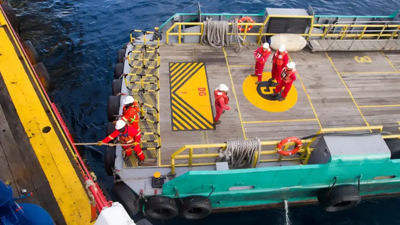 Équipage en combinaison rouge ajustant la longueur du bout de remorquage du bateau. Ils travaillent sur le pont d'un navire, manœuvrant une corde.