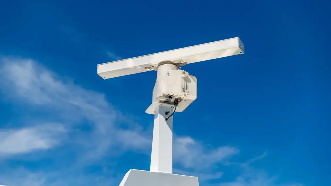 Antenne blanche sur un mât, sous un ciel bleu. Elle ressemble à un radar, mais pourrait aussi servir pour la communication satellite.