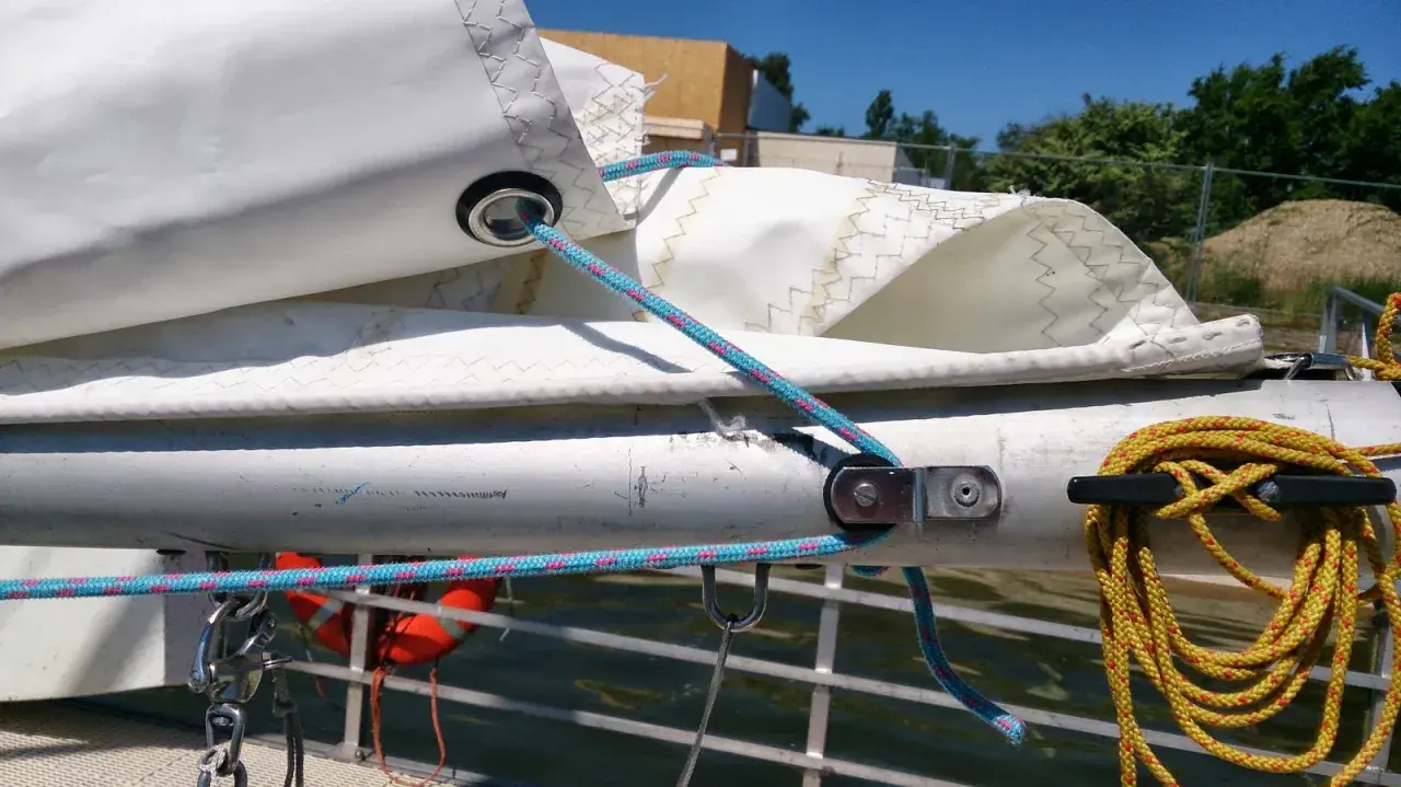 Poulie pour prise de ris automatique sur un mât de bateau, avec des cordages bleus et roses.