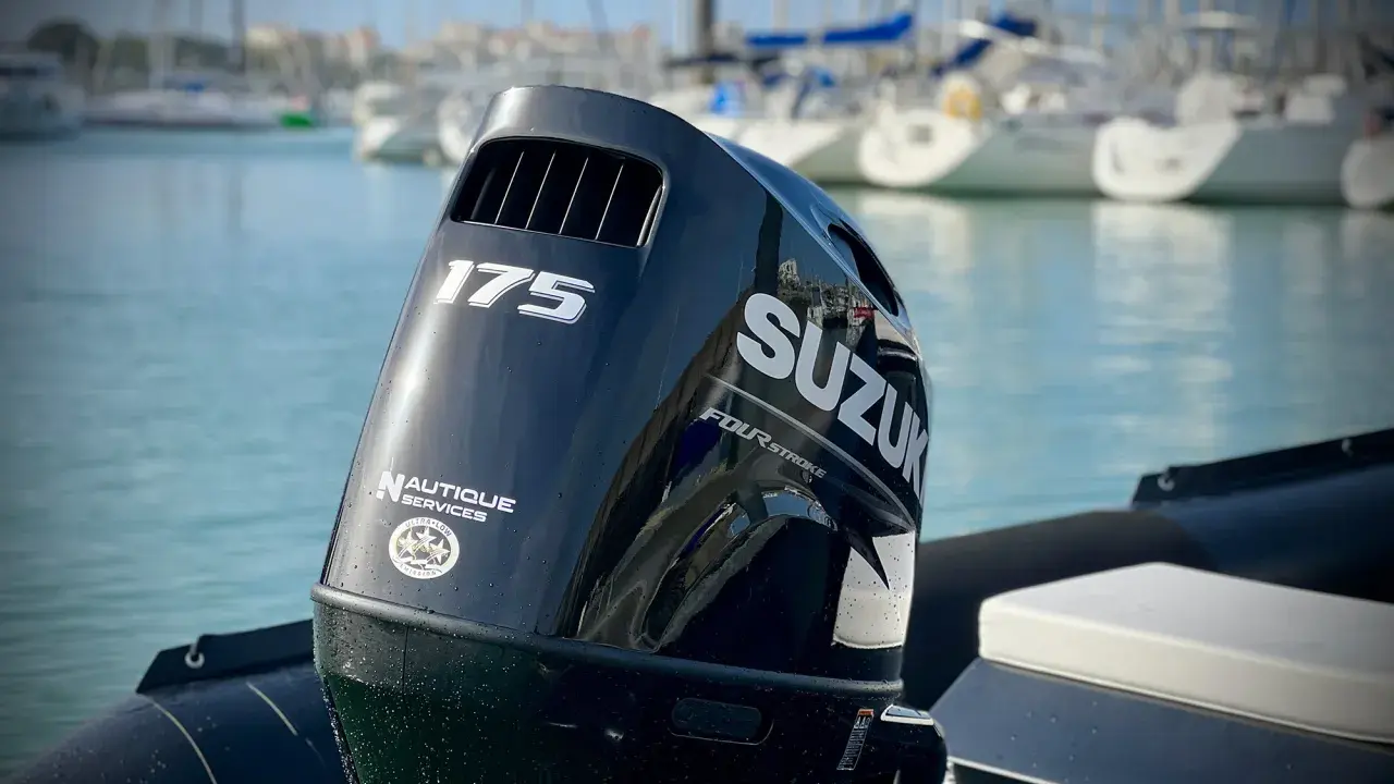 Moteur hors-bord Suzuki 175 CV, prêt pour une longue journée sur l'eau. Le mât de l'arbre est visible, avec des voiliers en arrière-plan.