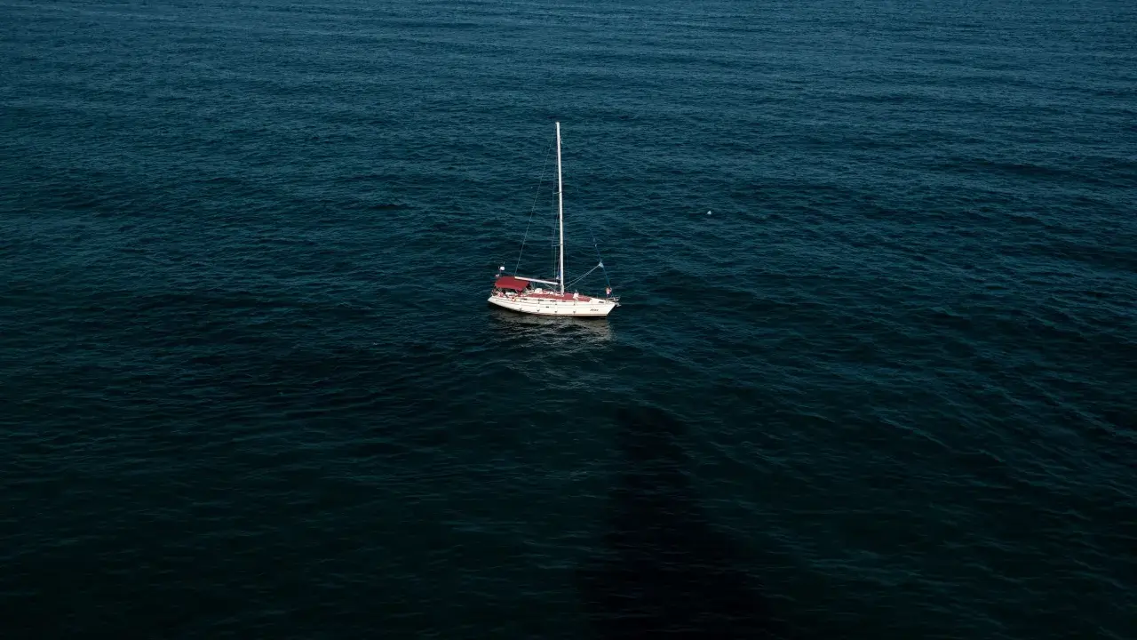 Un voilier blanc et rouge est au mouillage sur une mer sombre. La question est : combien de temps peut on rester au mouillage dans ce décor paisible ?