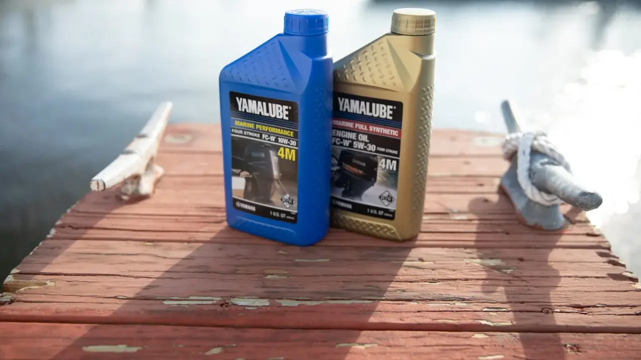 Deux bidons d'huile Yamalube pour moteur 4 temps, l'un bleu (10W-30) et l'autre doré (5W-30), sur un ponton en bois.