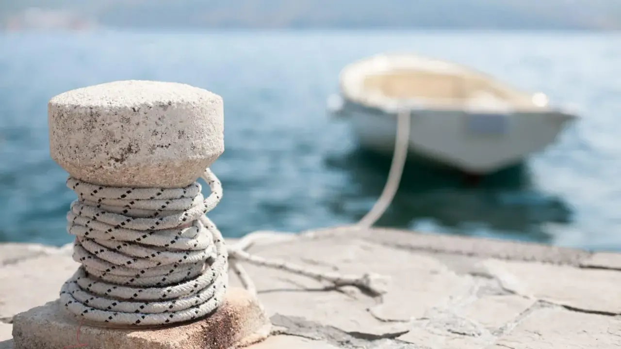Gros plan sur un bollard en pierre avec une corde enroulée, prêt pour l'attache bateau pour quai. Un petit bateau est amarré en arrière-plan.