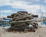 Grosse amarre enroulée sur une bitte d'amarrage, prête à supporter le poids d'un bateau. Le diamètre de la corde suggère une grande résistance.