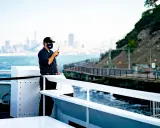 Un homme sur un bateau utilise une radio. Il est en communication, peut-être sur une fréquence vhf libre, avec la ville en arrière-plan.