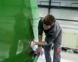 Un ouvrier polit la coque d'un bateau en polyester vert vif dans un atelier.