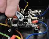 Main d'un technicien manipulant un connecteur sur un bornier électrique. Le moteur électrique chauffe et s'arrête, nécessitant une vérification des connexions.