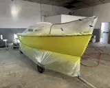 Un bateau jaune est bâché pour le repeindre. Il est sur une remorque dans un atelier.