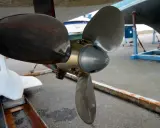 Gros plan sur l'hélice d'un bateau, prête pour son nettoyage. Une autre hélice blanche est visible à gauche.