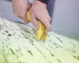 Mains utilisant un grattoir électrique antifouling pour enlever des résidus verts sur une surface.