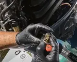 Mains gantées tenant un thermostat usagé, prêt pour le changement sur un moteur hors bord Yamaha.
