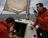 Deux hommes sur un voilier en mer agitée examinent le moteur. L'un éclaire avec une lampe torche, l'autre tient une clé, peut-être pour le fonctionnement inverseur moteur bateau.