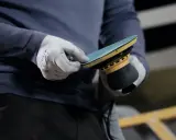 Gants blancs ajustant un disque sur une ponceuse Mirka, prêt à polir la coque d'un bateau.