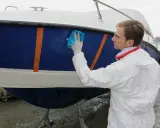 Un homme en combinaison blanche effectue l'entretien d'un bateau bleu et blanc, le lustrant avec un chiffon bleu.