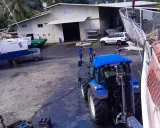 Tracteur bleu près d'un bateau, peut-être pour le prix d'entretien d'un bateau de 7m. Des ouvriers travaillent.