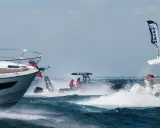 Trois bateaux en pleine navigation, éclaboussures d'eau, ciel bleu. L'un d'eux, un Zodiac, fend les vagues avec deux personnes à bord.