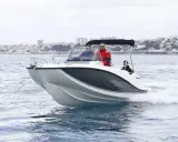 Bateau blanc et gris naviguant sur l'eau, avec trois personnes à bord. Le tableau de bord indique la puissance du moteur du bateau. Ville en arrière-plan.