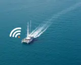 Un catamaran à voile navigue sur une mer bleue, avec un symbole de connexion Wi-Fi à proximité.