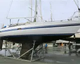 Un grand voilier blanc et bleu est sur des chandelles, son flanc couvert de bernacles. Un homme nettoie la coque d'un autre bateau à proximité.