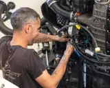 Un mécanicien s'affaire sur un moteur électrique, câbles et tuyaux visibles. Il sait comment tester un moteur électrique pour assurer son bon fonctionnement.