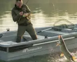 Pêcheur joyeux dans une barque, un brochet saute hors de l'eau. L'image évoque l'idée de fabriquer un poids pour barque, essentiel pour la stabilité lors de telles prises.