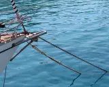 L'étrave d'un voilier blanc est ancrée dans une eau bleue et claire. La chaîne et la corde sont bien visibles, prêtes à mouiller beaucoup.