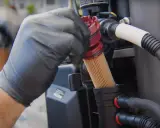 Main d'un mécanicien en gant noir retirant un filtre à gasoil encrassé, conséquence d'un mauvais entretien.