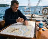 Un homme utilise un compas de marine pour lire une carte nautique sur un voilier.