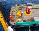 Équipage en combinaison rouge ajustant la longueur du bout de remorquage du bateau. Ils travaillent sur le pont d'un navire, manœuvrant une corde.