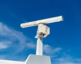 Antenne blanche sur un mât, sous un ciel bleu. Elle ressemble à un radar, mais pourrait aussi servir pour la communication satellite.