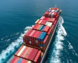 Un immense porte-conteneurs navigue sur une mer bleue, témoignant du **trafic maritime** mondial. Des conteneurs colorés s'empilent sur le pont.