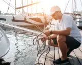 Un homme prépare une corde sur un ponton, près d'un bateau. Il manipule le cordage, peut-être pour un système de poulie.