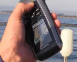 Main tenant une carte GPS Garmin sur un bateau, naviguant sur l'eau.