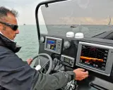 Un homme navigue, consultant un écran de sonar affichant des données sous-marines.