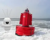 Deux bouées, une blanche avec des antennes et une rouge marquée "P8", flottent sur l'eau agitée, un petit bateau à l'horizon.