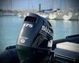 Moteur hors-bord Suzuki 175 CV, prêt pour une longue journée sur l'eau. Le mât de l'arbre est visible, avec des voiliers en arrière-plan.