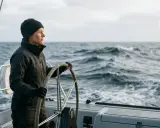 Une femme au gouvernail, concentrée sur la mer agitée. Elle sait comment prendre les vagues en bateau, naviguant avec assurance.