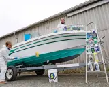Un homme en combinaison blanche nettoie le flanc d'un bateau blanc et vert sur une remorque. Le nettoyage du pont du bateau est en cours.