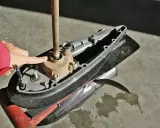 Main d'une personne en veste rouge pointant vers la turbine d'un moteur hors-bord Yamaha 2 temps, prêt à changer la pièce.