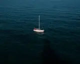 Un voilier blanc et rouge est au mouillage sur une mer sombre. La question est : combien de temps peut on rester au mouillage dans ce décor paisible ?