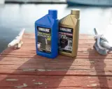Deux bidons d'huile Yamalube pour moteur 4 temps, l'un bleu (10W-30) et l'autre doré (5W-30), sur un ponton en bois.