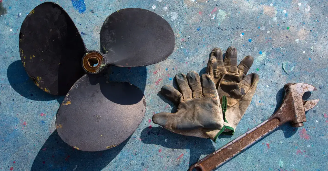 Hélice de bateau, gants usés et clé rouillée, prêts pour la révision moteur bateau.