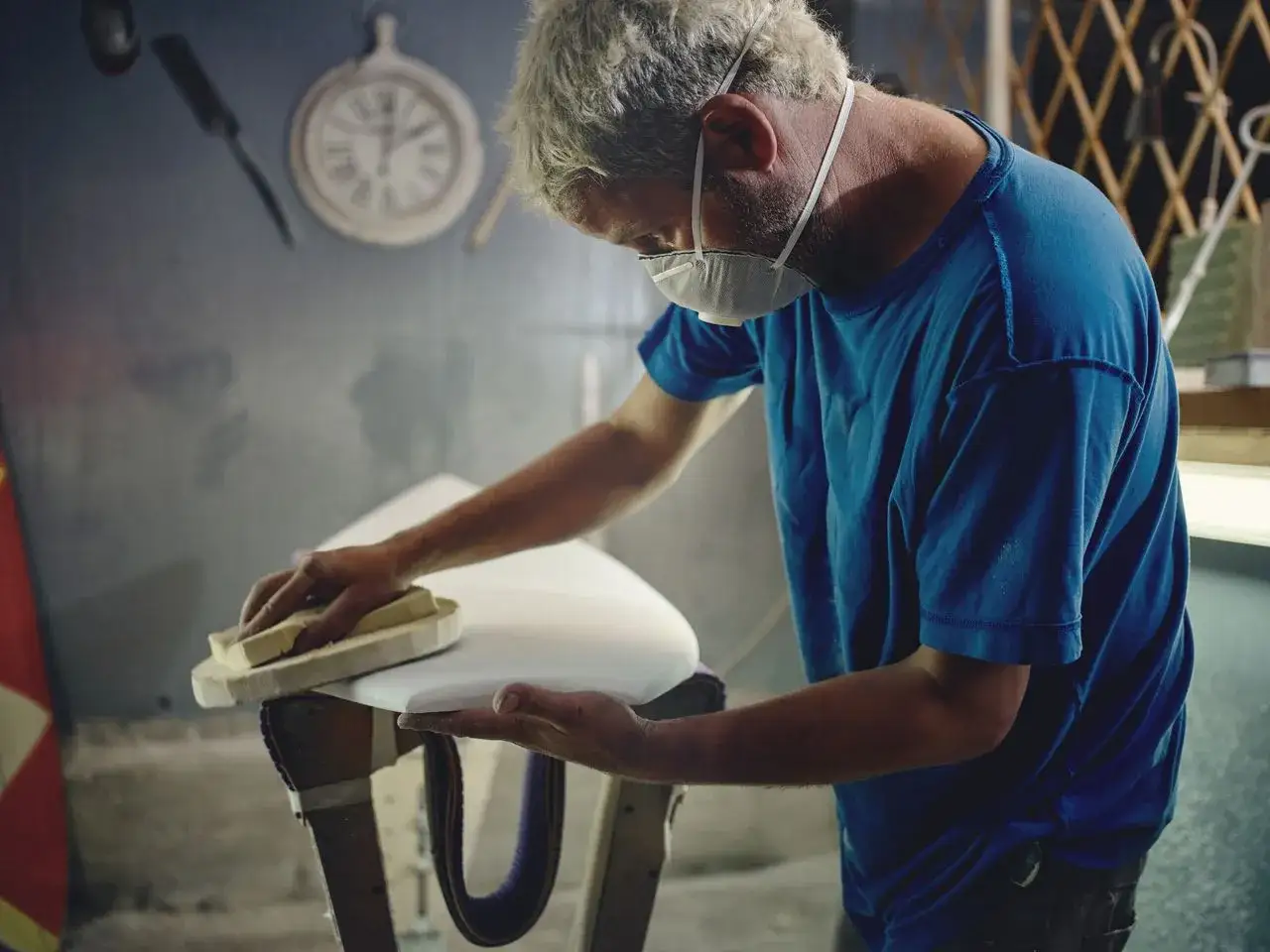 Artisan ponçant une planche de surf blanche, application d'epoxy sur polyester.