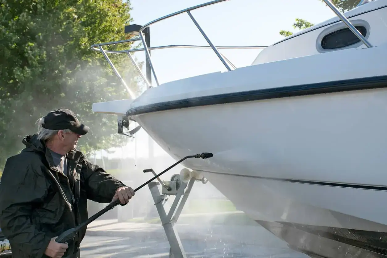 Un homme utilise un nettoyeur haute pression pour comment laver une coque de bateau blanche.