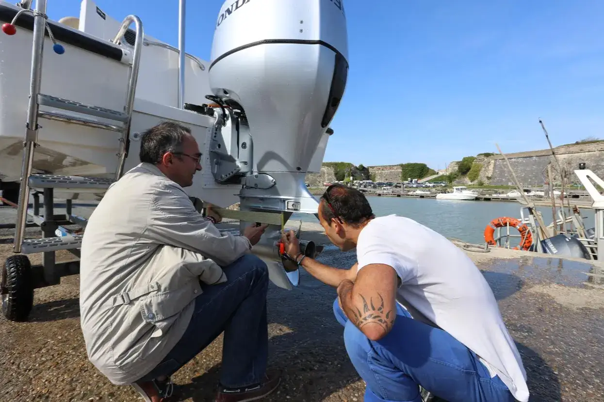 Deux hommes mesurent la longueur de l'arbre du moteur hors bord d'un bateau, près d'un port.