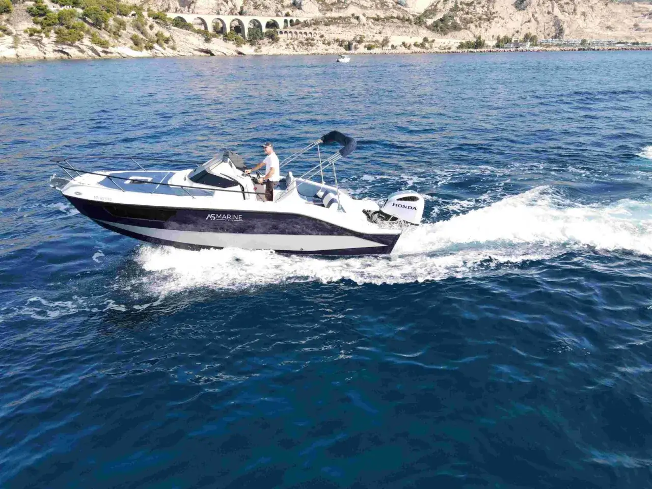 Un homme pilote un bateau AS Marine de 7m sur une mer bleue, propulsé par un moteur Honda. Le choix du bon moteur est crucial pour un bateau de 7m.